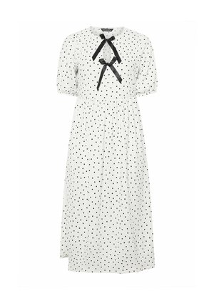 Vestido midi blanco con lunares negros, mangas cortas abullonadas, escote redondo y dos lazos de cinta negra en el pecho.