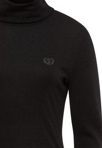 Black turtleneck top in a soft, stretchy fabric. Features a small, rhinestone-studded heart logo on the left chest.
