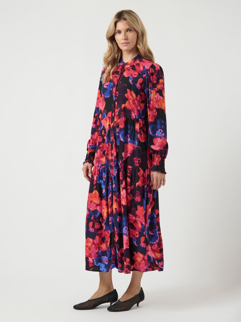 Kwiatowa sukienka z długim rękawem i wielowarstwowym dołem. Posiada intensywne czerwone, różowe i niebieskie wzory na czarnym tle. Wykonana z lekkiego materiału.