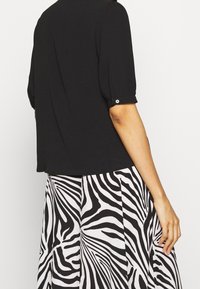 Blouse noire à manches courtes bouffantes, associée à une jupe blanche avec un motif zèbre noir prononcé. Texture de tissu lisse.