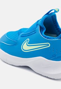 Baskets de sport bleu avec un dessus synthétique lisse, présentant un swoosh Nike vert clair, une boîte à orteils texturée et une semelle en caoutchouc blanc.