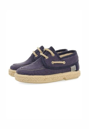 Zapatos de barco de lona azul marino con cordones en tono beige claro y suela de yute trenzado. Presentan un parche con el logo en el lateral y costuras a lo largo del borde superior.