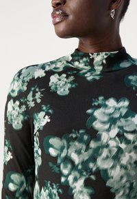 Zwarte blouse met lange mouwen met een bloemenpatroon in groene en witte tinten. Glad materiaal met een hoge halslijn en een aansluitende pasvorm.