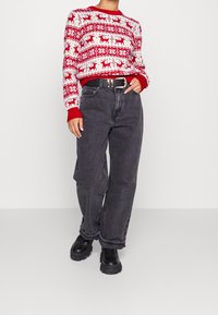 Roter und weiß gemusterter Pullover mit Rentiermotiv, kombiniert mit hoch taillierten dunkelgrauen Jeans und schwarzen klobigen Stiefeletten.