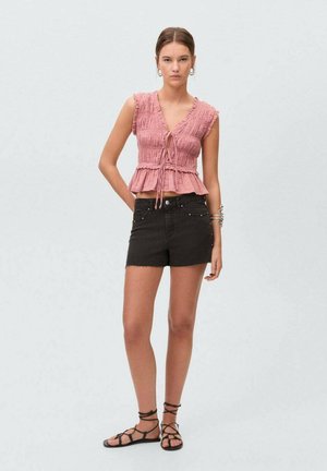 Rosa, texturiertes, ärmelloses Oberteil mit vornem Bindeband und gerafften Rändern, kombiniert mit schwarzen Jeansshorts und schwarzen Riemchensandalen.