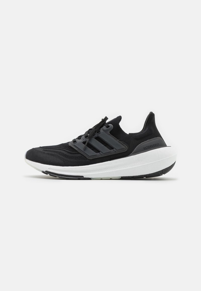Chaussures de sport noires avec une tige en tricot, accents gris à trois bandes et une semelle blanche épaisse avec une semelle extérieure noire texturée.