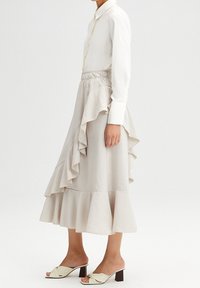 Camisa blanca de manga larga con una tapeta de botones amarilla combinada con una falda larga beige con volantes. Se lleva con zapatos mule verde claro con tacón bloque.