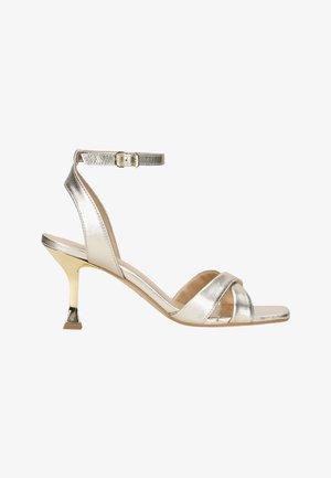 Metallic silberne Absatzsandalen mit einem Knöchelriemen, offener Zehenpartie und überkreuztem Design. Mit einem goldfarbenen Absatz und glatter Textur.