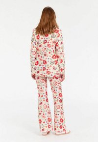 Costume à imprimé floral en crème, comprenant des manches longues et un pantalon évasé. Le design inclut des fleurs rouges, roses et bleues avec des accents détaillés.