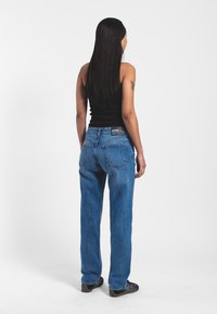 Jeans in denim azzurro chiaro, a gamba dritta, vita media, con tasche posteriori. Indossati con un top nero senza maniche. Design semplice, con dettagli minimi.