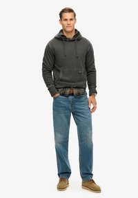 Gray hoodie with front pocket, layered over a plaid flannel shirt. Light blue jeans and tan shoes complete the outfit.