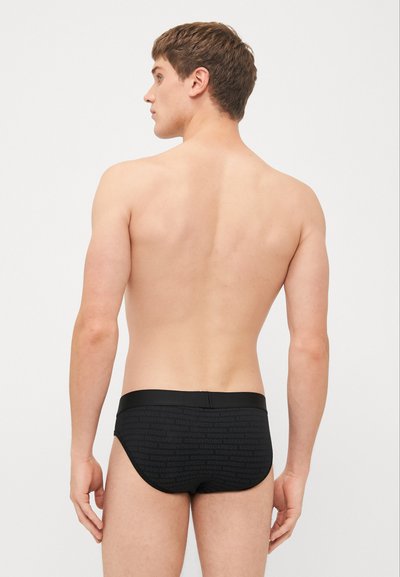 Schwarze Schwimmslips aus glattem Material, mit einem sich wiederholenden Logo-Muster. Der Bund ist elastisch und sorgt für eine enge Passform.
