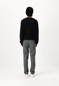 Maglione nero a trama waffle con vestibilità ampia, abbinato a pantaloni grigi eleganti e sneakers bianche, visto da dietro.