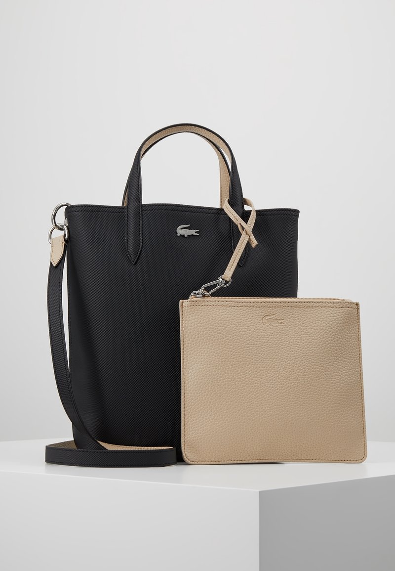 Sac fourre-tout noir avec finition texturée, anses doubles et pochette zippée beige. Accent logo argenté à l'avant. Matériaux lisses et durables.
