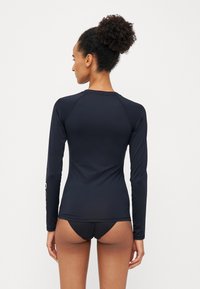 Top da costume a maniche lunghe di colore blu navy scuro, realizzato in un tessuto morbido e elasticizzato. Presenta un design aderente con scollatura rotonda e maniche raglan.