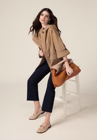 Giubbotto beige con cappuccio e dettagli a bottoni, pantaloni cropped navy e mocassini beige con un accento dorato. Borsa marrone con un design strutturato.