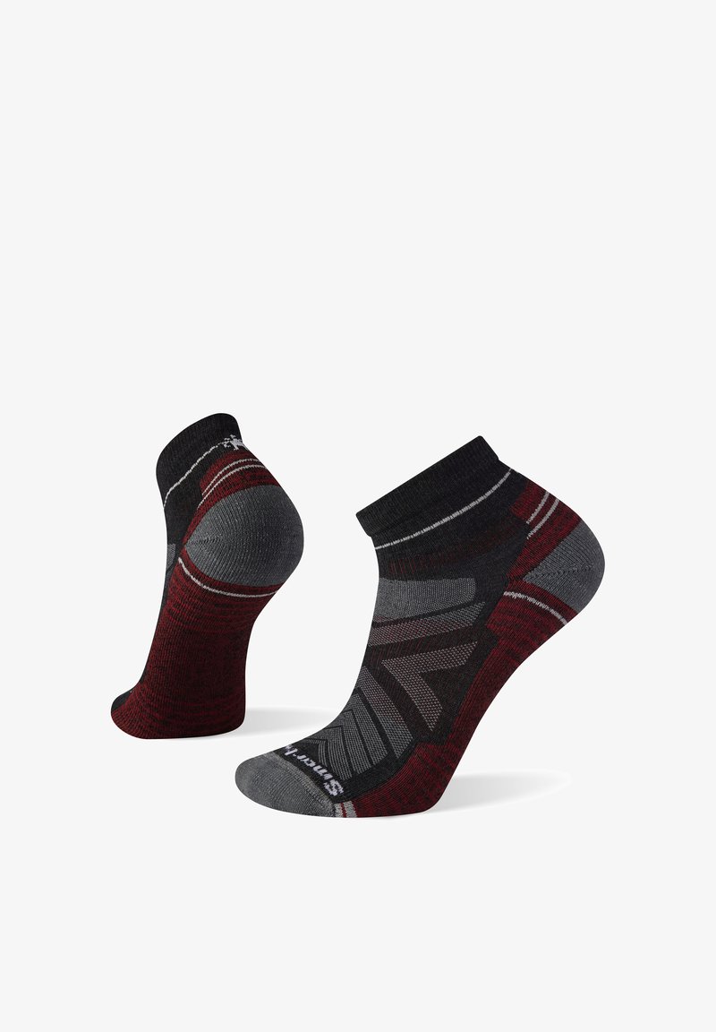 Coppia di calzini sportivi a taglio basso in nero, grigio e rosso scuro con motivi geometrici e zone imbottite su tallone e punta.