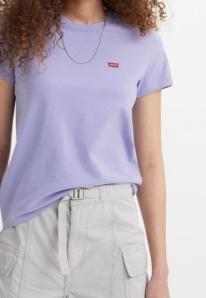 Personne portant un t-shirt Levi's lavande, un pantalon cargo gris clair avec une ceinture en tissu et un collier chaîne fin, visible du cou jusqu'aux hanches.