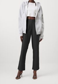 Šedá mikina na zip, bílý cropped top, černé široké kalhoty a černé sandály na podpatku. Hladké textury a uvolněný střih po celém outfitu.