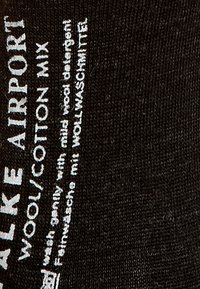 Calcetines negros fabricados con una mezcla de lana y algodón, que presentan texto impreso en blanco con instrucciones de cuidado y el nombre del producto. Textura suave.