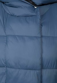 Marinblå pufferjacka med quiltade sektioner, glänsande tygtextur, hög krage och tryckknappsstängning vid nacken.