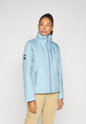Giacca impermeabile azzurro chiaro con collo alto, cerniera frontale e due tasche laterali. Presenta una toppa con logo sulla manica sinistra.