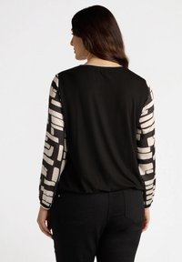 Musta paita, jossa on kuvioidut, puoliksi läpinäkyvät pitkät hihat beigen ja mustan värisinä. Pehmeä materiaali, pyöreä kaula-aukko ja rento istuvuus selässä.