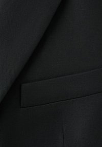 Primo piano di tessuto nero strutturato per abito che mostra la rever della giacca e una tasca a filetto con dettagli di tessitura fine.