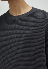 Ciemnoszary sweter z dzianiny o fakturowanym, prążkowanym wzorze i klasycznym, okrągłym dekolcie. Tkanina wydaje się miękka i ciepła.