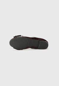 Semelle de chaussure rouge à motifs avec des rainures en caoutchouc texturé, dotée d'un bord noir et d'une forme plate. Comprend un détail de sangle pour la fermeture.