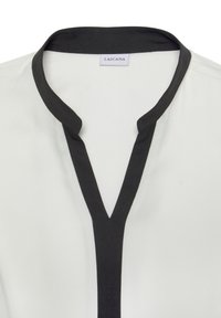 Witte blouse met een V-vormige halslijn en een contrasterende zwarte kraag. De stof lijkt soepel, wat het minimalistische ontwerp benadrukt.