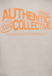 Light gray t-shirt featuring bold orange text: "AUTHENTIC YOUNG COLLECTIVE" and additional small print below, with a standard crew neckline.