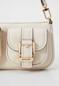 Light beige leather handbag featuring a gold-tone buckle closure, dual front pockets, and a detachable shoulder strap. Textured surface.