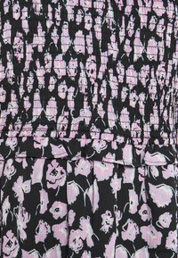 Tissu noir avec motif floral abstrait rose clair et blanc et partie supérieure smockée froncée passant à une partie inférieure ample.