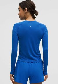 Sinine pikkade varrukatega spordipusa tekstuuriga viimistlusega, millel on sujuv õlavarre disain ja väike logo detail seljal.