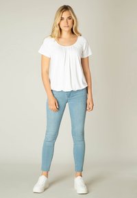 Witte top met korte mouwen en een ronde halslijn, met plooien aan de voorkant, gecombineerd met lichtblauwe skinny jeans en witte sneakers.