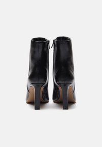 Bottines en cuir noir avec une texture lisse, des talons aiguilles hauts et des fermetures éclair sur le côté, présentant un design minimaliste.