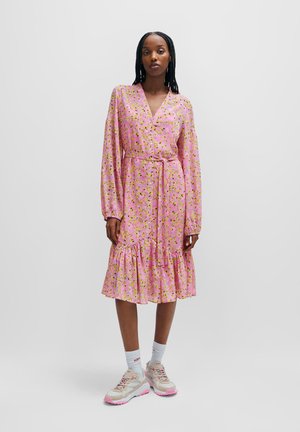 Pink floral wrap dress with long sleeves, ruffled hem, and matching tie belt, paired with chunky sneakers and ankle socks.