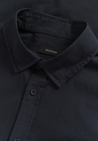 Chemise bleu marine foncé à col en tissu lisse. Présente une fermeture à boutons et une étiquette de marque "Matinique" au niveau du col.