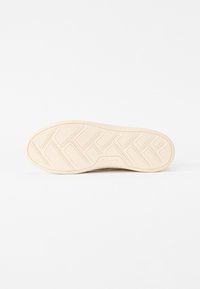 Semelle de chaussure en caoutchouc beige clair avec un design de grip texturé et à motifs, finition lisse et logo de la marque en relief.
