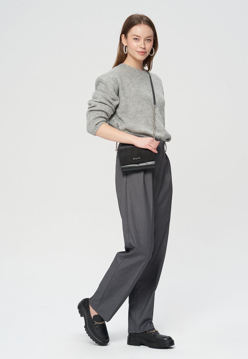 Szary sweter z dzianiny, szare plisowane spodnie, czarna torebka na ramię oraz czarne loafersy z detalem w postaci łańcucha. Czyste linie i teksturowane materiały.