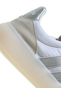 Baskets blanches avec des accents en daim et en cuir gris et argent. Dotées d'une semelle translucide et de détails cousus sur le dessus.