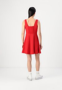 Robe rouge avec un corsage ajusté et une jupe évasée. Présente un dos carré et un panneau texturé. Assortie à des baskets montantes blanches.