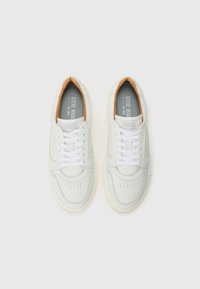 Zapatillas de cuero blancas con una textura suave, punta redondeada y plantilla de color tostado en contraste. Cuentan con cordones blancos y detalles perforados en la puntera.