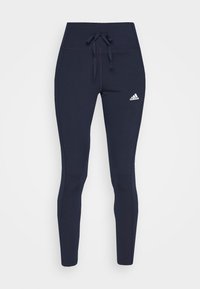 Granatowe legginsy z wysokim stanem i sznurkiem w talii, wykonane z elastycznego materiału, z białym logo Adidas na lewym udzie.