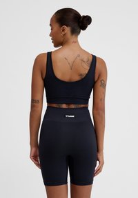 Zwarte, aansluitende atletische crop top en high-waisted shorts gemaakt van textuurstof met rek. Bevat een merkembleem op de tailleband.
