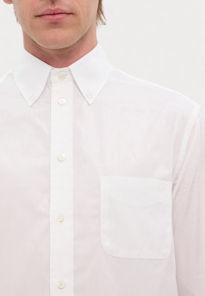 White button-up shirt with a structured collar, front pocket, and subtle brand logo. Made of smooth fabric with a polished finish.