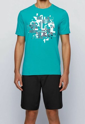 Türkisfarbenes kurzärmeliges T-Shirt aus Baumwolle mit einem grafischen Design in Weiß und Grau, kombiniert mit schwarzen Shorts.
