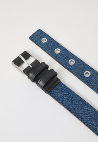 Cinturón de mezclilla azul oscuro con herrajes plateados, que cuenta con una sección de piel negra y ojetes a lo largo para ajustar.