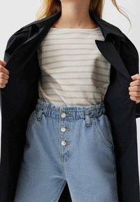 Camiseta de rayas beige y blanca debajo de un abrigo negro; jeans de mezclilla azul claro de cintura alta con cintura elástica y cierre de tres botones.